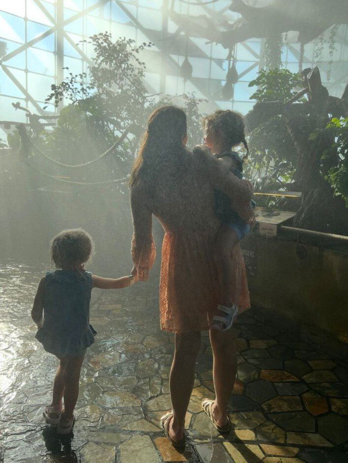 Mutter geht mit zwei Kindern durch ein Tropenhaus, eines trägt ein Cochlea Implantat.