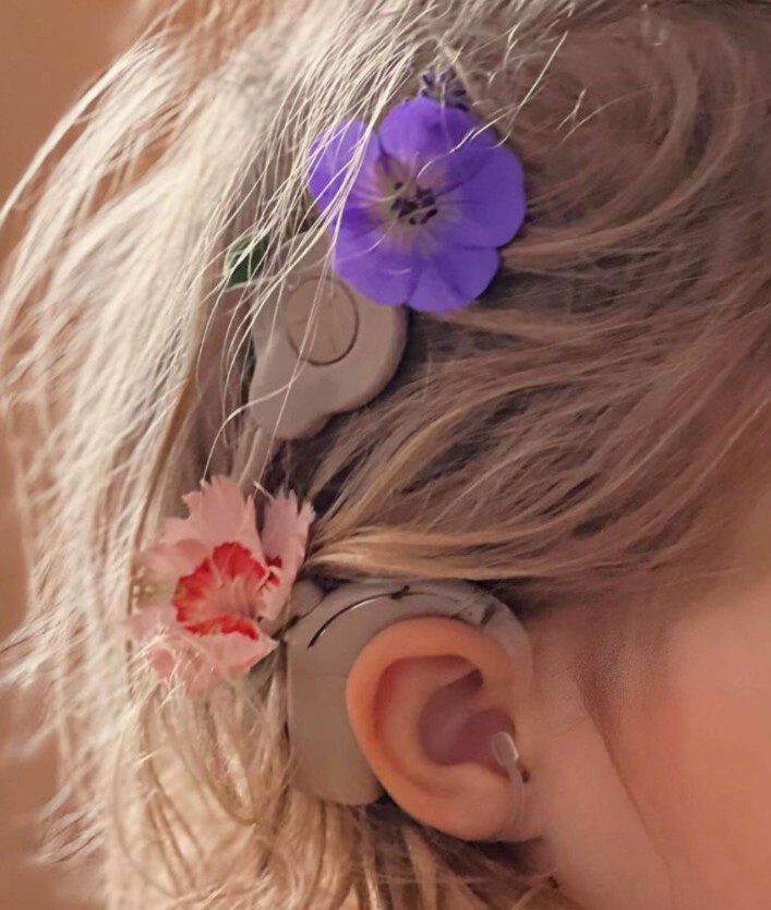 Kind mit Hörgerät und Blumen im Haar.