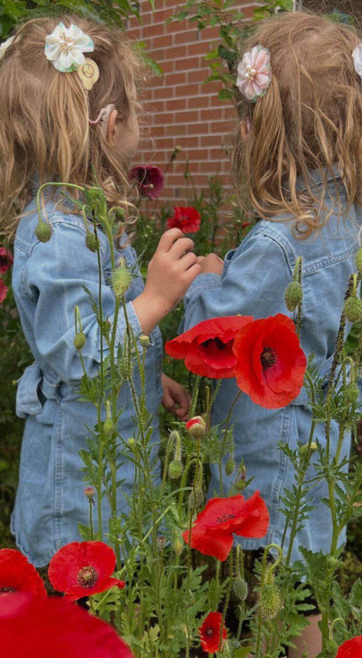 Zwei Mädchen mit Hörhilfen stehen zwischen roten Mohnblumen.