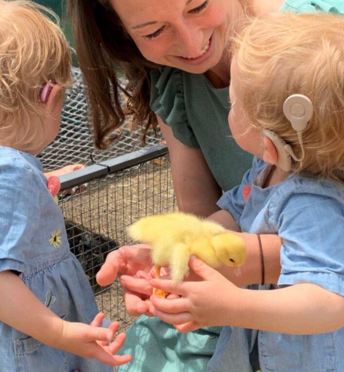 Kinder mit Hörhilfen halten gemeinsam ein Küken.